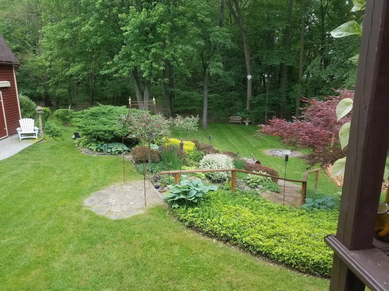 Mowed backyard lawn framed by woodland garden beds and a flagstone path