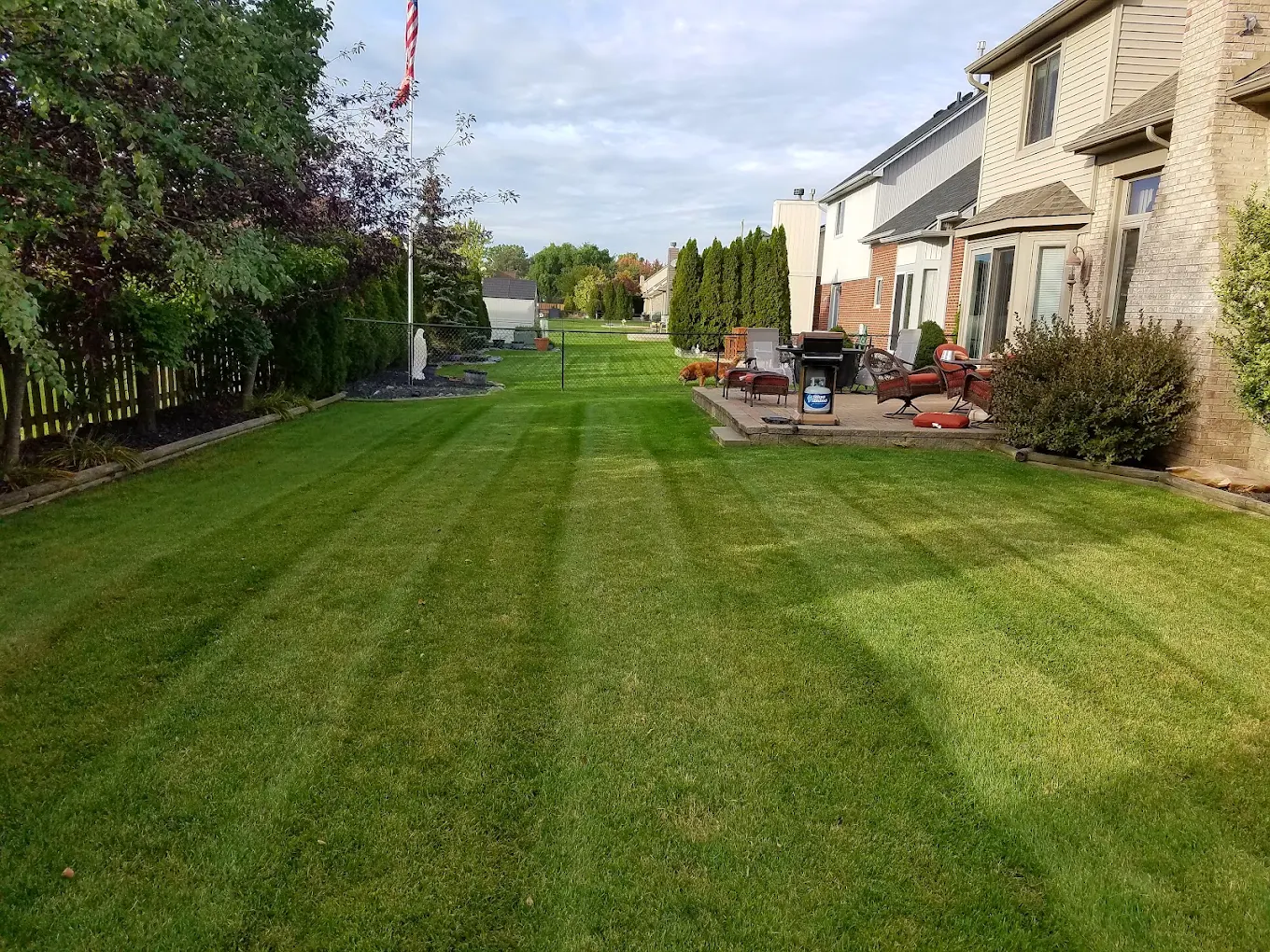 Striped backyard lawn beside a stone patio with fire pit and seating