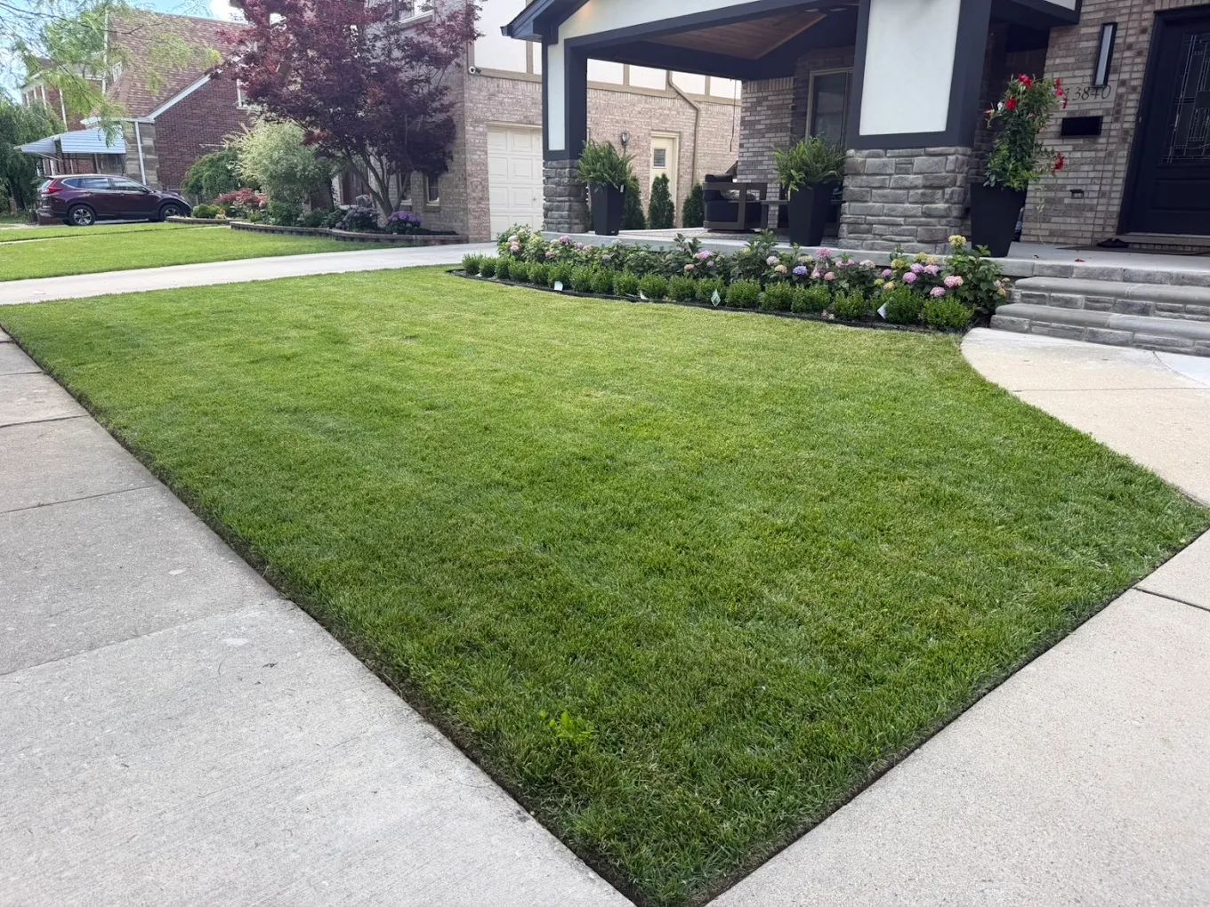 Manicured front lawn with clean edging and flower beds beside a stone home