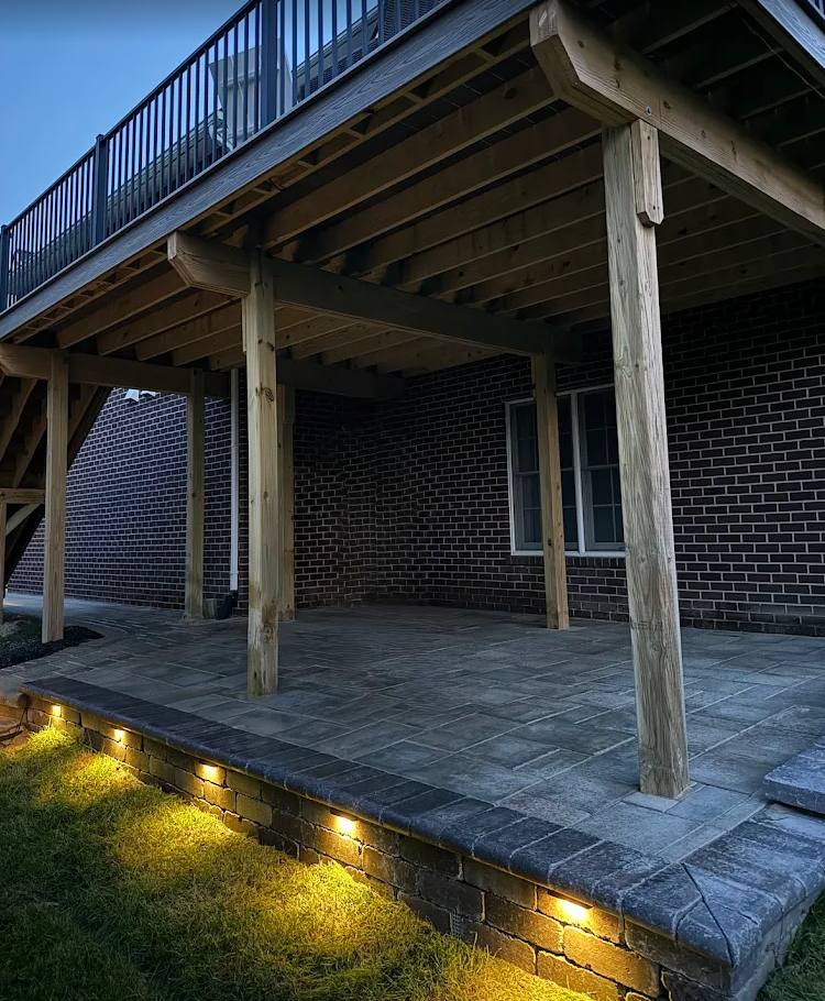Paver patio under a raised deck with lit stone facing