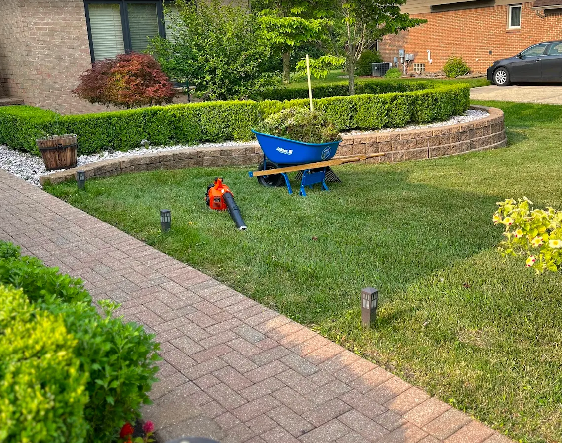 Lawn maintenance in progress with equipment beside a paver walkway