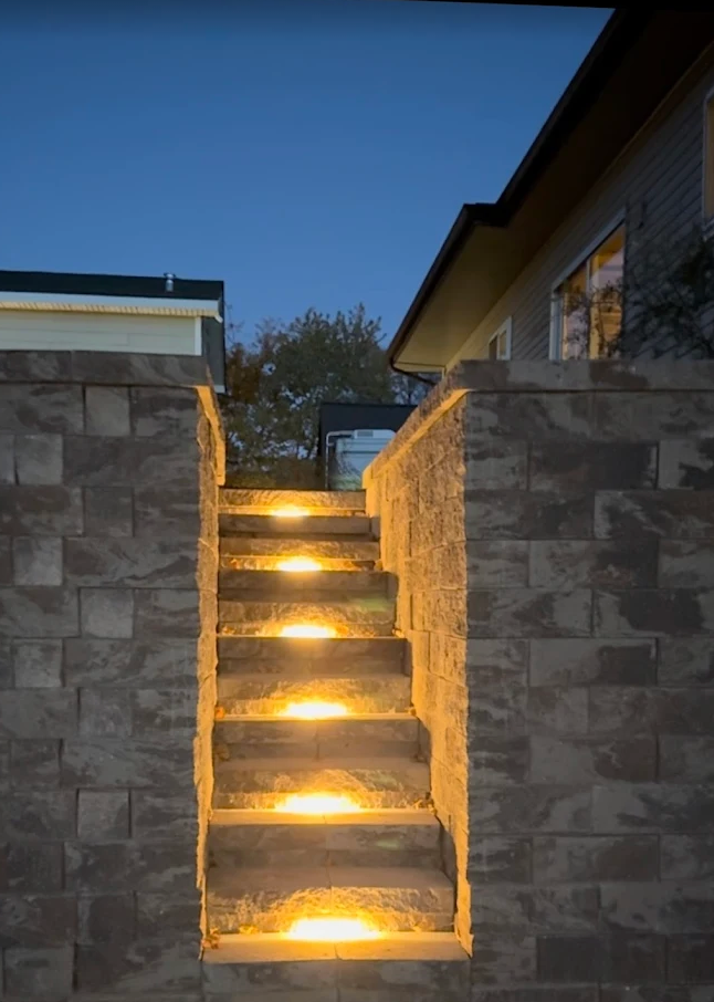Illuminated stone steps between block retaining walls at dusk