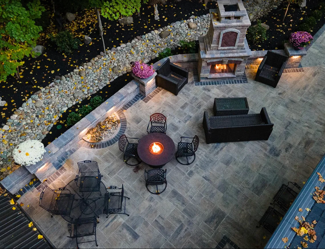 Aerial view of a paver patio with fire table, seating wall, and outdoor stone fireplace